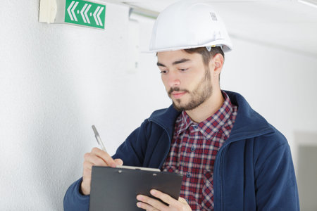 inspector next to fire escape sign making notes on clipboard
