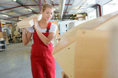 pretty young woman carrying wood in a workshopの写真素材