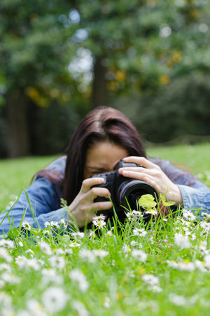 female photographer laid on the grass to capture shotの写真素材