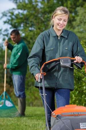 female worker using a lawn mower for cutting green grass