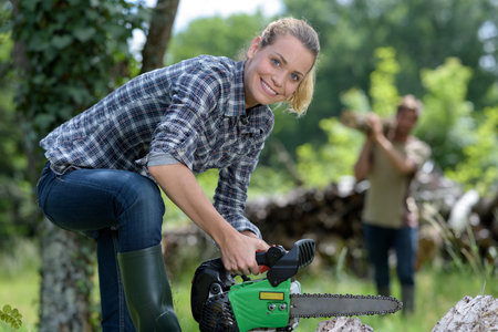 woman with chainsaw is sawing a logの写真素材