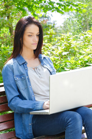 cheerful pretty young woman using laptop on bench outdoorsの写真素材