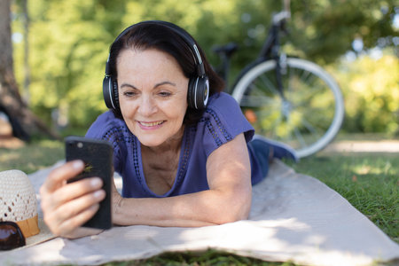 mature woman listening to music while laying on the grassの写真素材