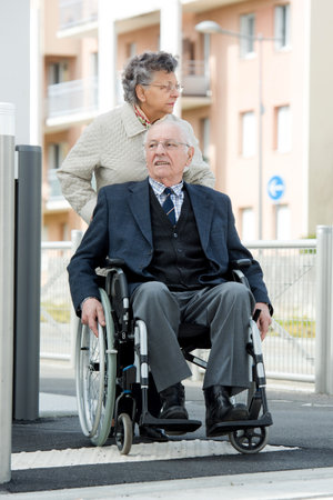 senior man in wheelchair being pushed by wifeの写真素材