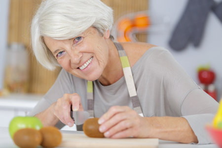 senior woman cutting tomatoes in kitchenの写真素材