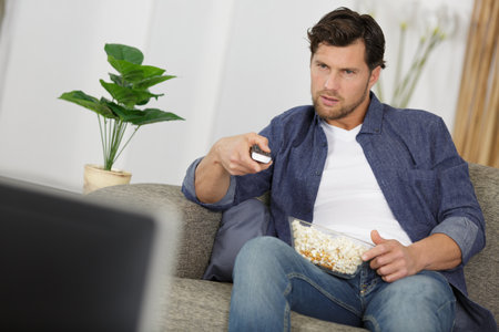 man on the sofa watching a movie with popcornの写真素材