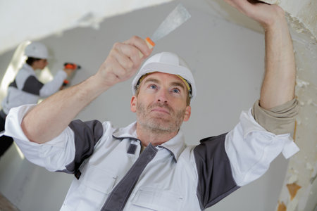 worker spreading plaster on ceiling at construction siteの写真素材