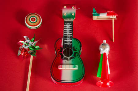 Yo yo, toy windmill, guitar, toy trumpet and noisemaker against red background. Accessories for mexican Independence Day celebrationの写真素材