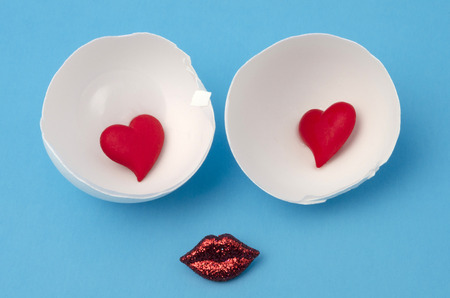 Cute face made from eggshells with little red hearts in the center and red lips against blue backgroundの写真素材
