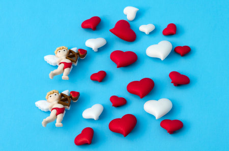 Two little cupids and a few little red and white hearts against blue background