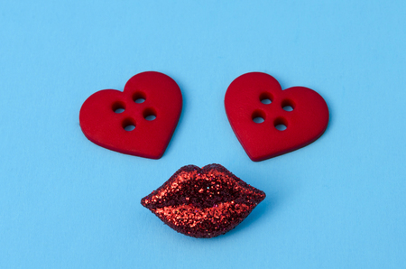 Cute face made from two red heart shape buttons and red lips against blue backgroundの写真素材