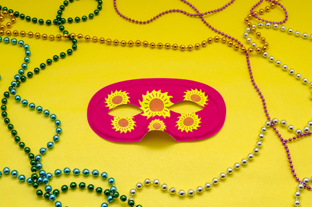 Party pink eye mask and colorful mardi gras beads against yellow backgroundの写真素材