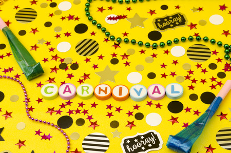 Top view decoration for party. Word carnival made from colorful letters, plastic necklaces, party blowers and circles and stars confetti on yellow backgroundの写真素材