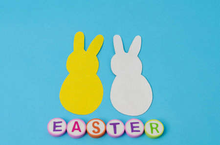 Yellow and white paper bunnies and easter made form colorful letters on blue background