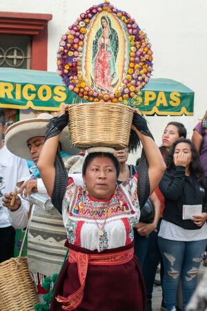 OAXACA, OAXACA, MEXICO- JULY 6, 2019: Woman dressed with traditional clothes dancing with a basket and the Virgin of Guadalupe decorated with flowers, during the Convite, a party made for invite to a big traditional party called Guelaguetza in Oaxaca, Mexのeditorial素材