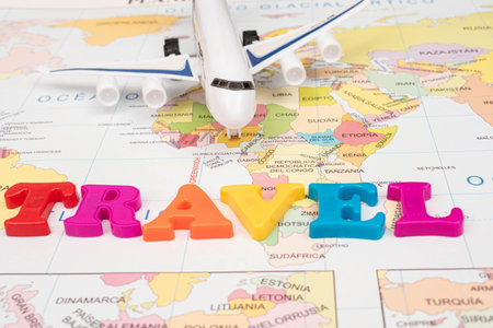 Toy airplane and the word travel made from colorful letters on a map as backgroundの写真素材