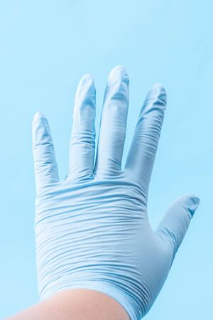 Extended hand in a blue glove on light blue backgroundの写真素材