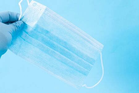 Hand with blue gloves holding a face mask on blue backgroundの写真素材