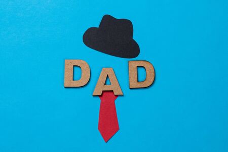 "Dad", word made from wooden letters, a little black hat and a red tie on blue backgroundの写真素材