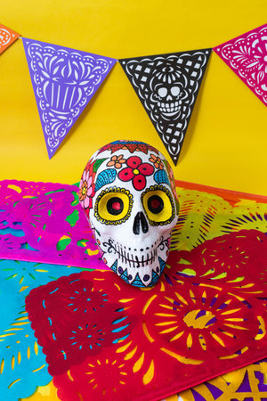 Hand painted skull, colorful day of the dead banner and colorful cut paper on yellow background