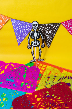 Articulated skeleton, a colorful day of the dead banner and cut paper on yellow background