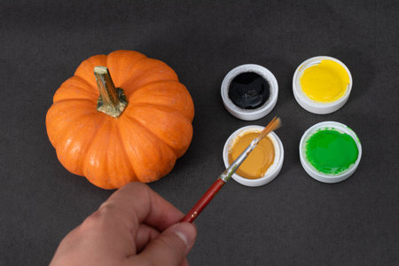 Woman hand holding a paint brush, little orange pumpkin and paints on black backgroundの写真素材