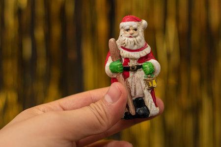 Woman hand holding a Santa Claus figurine on golden background. Christmas decoration