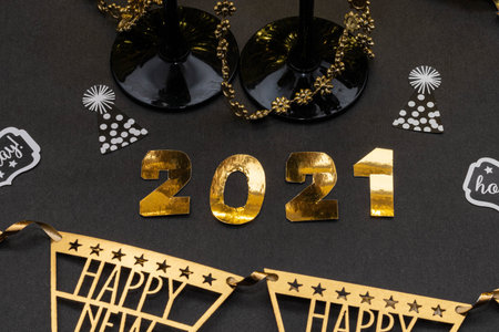 2021 made with golden numbers. Glasses, confetti and a banner on black background. New Year...
