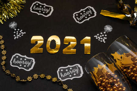 2021 made with golden numbers, glasses with golden balls and stars, confetti and ornaments on black background. New Year decorationの写真素材