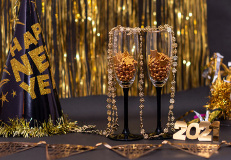 Two wine glasses with little golden balls and stars, 2021 made from golden numbers, New Year hat and...
