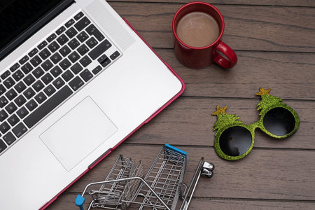 Flat lay photograph with a laptop, supermarket cart, red cup of coffee and christmas tree glasses on...