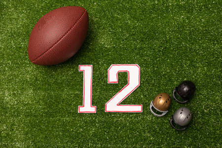 American football ball, number twelve and little helmets on green grass background. American football decorationの写真素材