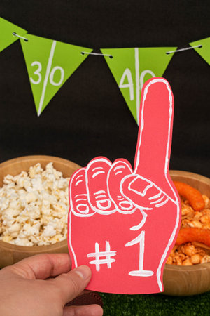 Woman hand holding a foam finger. Snacks and banner on black background. American football...