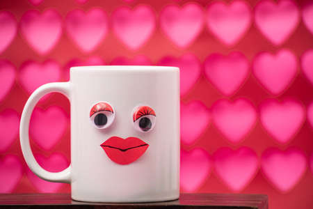 White mug with eyes and red lips on pink and red hearts background. Valentine's Day decorationの写真素材