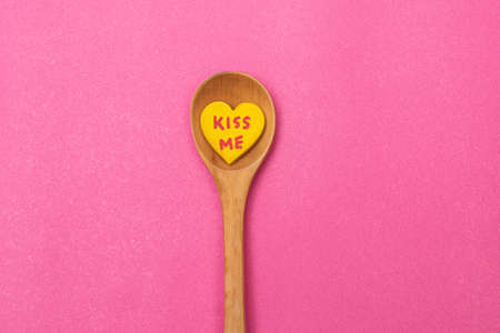 Wooden spoon in the middle, with little yellow heart with the phrase "kiss me", on pink backgroundの写真素材