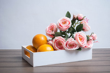 White box with oranges and pink roses on a wooden table and white backgroundの写真素材