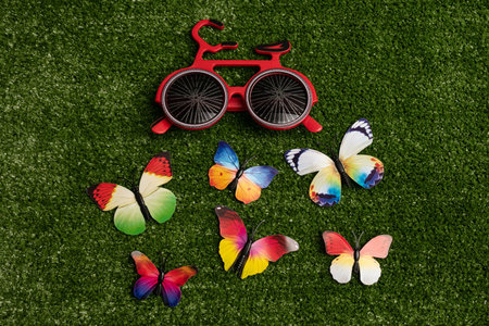 Red bike glasses and little colorful butterflies on green grass background