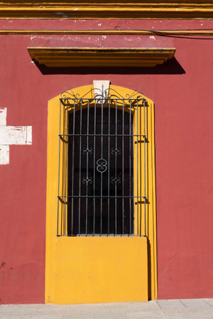 Iron window at a vivid red and yellow house at a sunny day