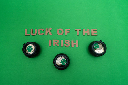 "Luck of the irish" made from wooden letters and three black pots full of golden coins and clovers on green backgroundの写真素材