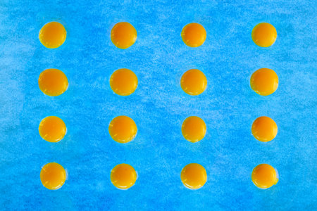 Pattern of egg yolks on blue textured background. Flat lay, top view.