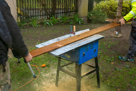 Two men cutting plank for terrace. Construction work in the yard.
