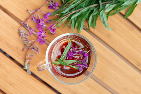 Fireweed herbal tea in the glass cup on wooden table with fresh fireweed flowers on background. Top view.の写真素材