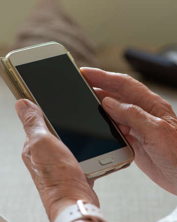 Hands of an senior woman holding blank screen smartphone. Close up. Copy space, mockup.の写真素材