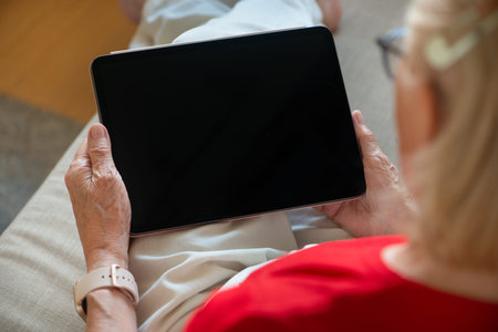 Senior woman holding blank screen tablet. Over the shoulder view. Copy space, mockup.