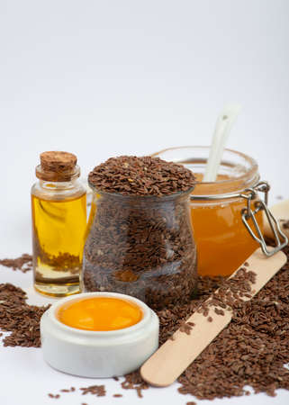 Brown flax seeds, linseeds oil, egg and honey on white background. Home made cosmetics ingredients.の写真素材