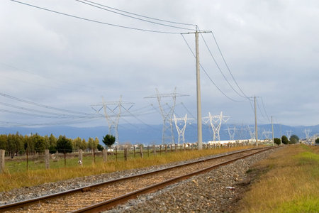A rail track leading into an industrial area surrounded by power transmission pylons