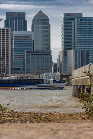 A cityscape of London viewed from across the River Thames featuring Canary Wharf and a boat passing the jettyのeditorial素材