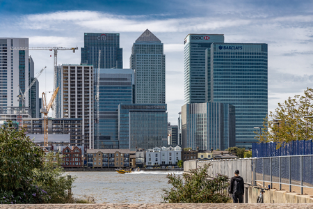 A cityscape of London viewed from across the River Thames featuring Canary Wharf and a boat passing the jettyのeditorial素材