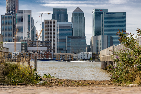 A cityscape of London viewed from across the River Thames featuring Canary Wharf and a boat passing the jettyのeditorial素材