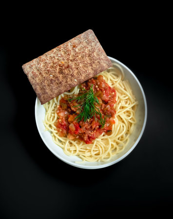 Pasta with tomato sauce in round bowl with cracker with dark background top view